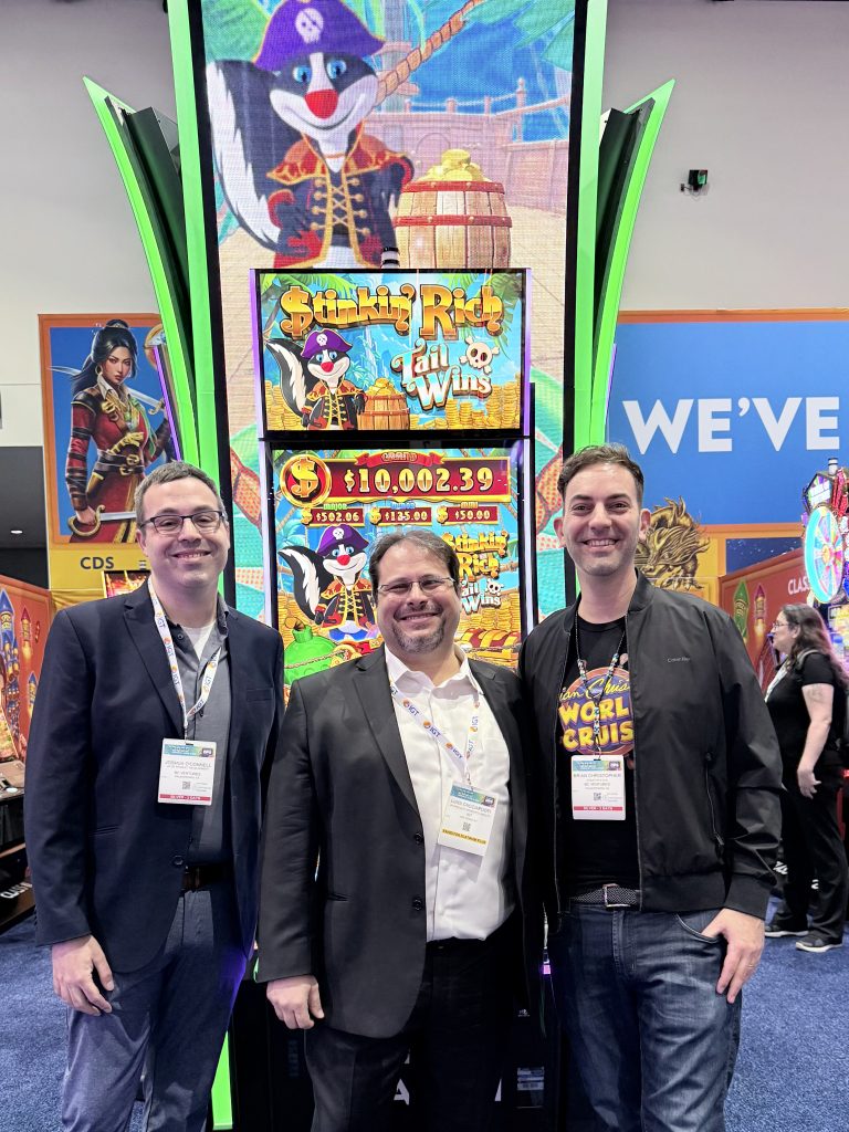 Josh O'Connell, Luigi Cacciapuoti, and Brian Christopher standing in front of Slot machine at IGA