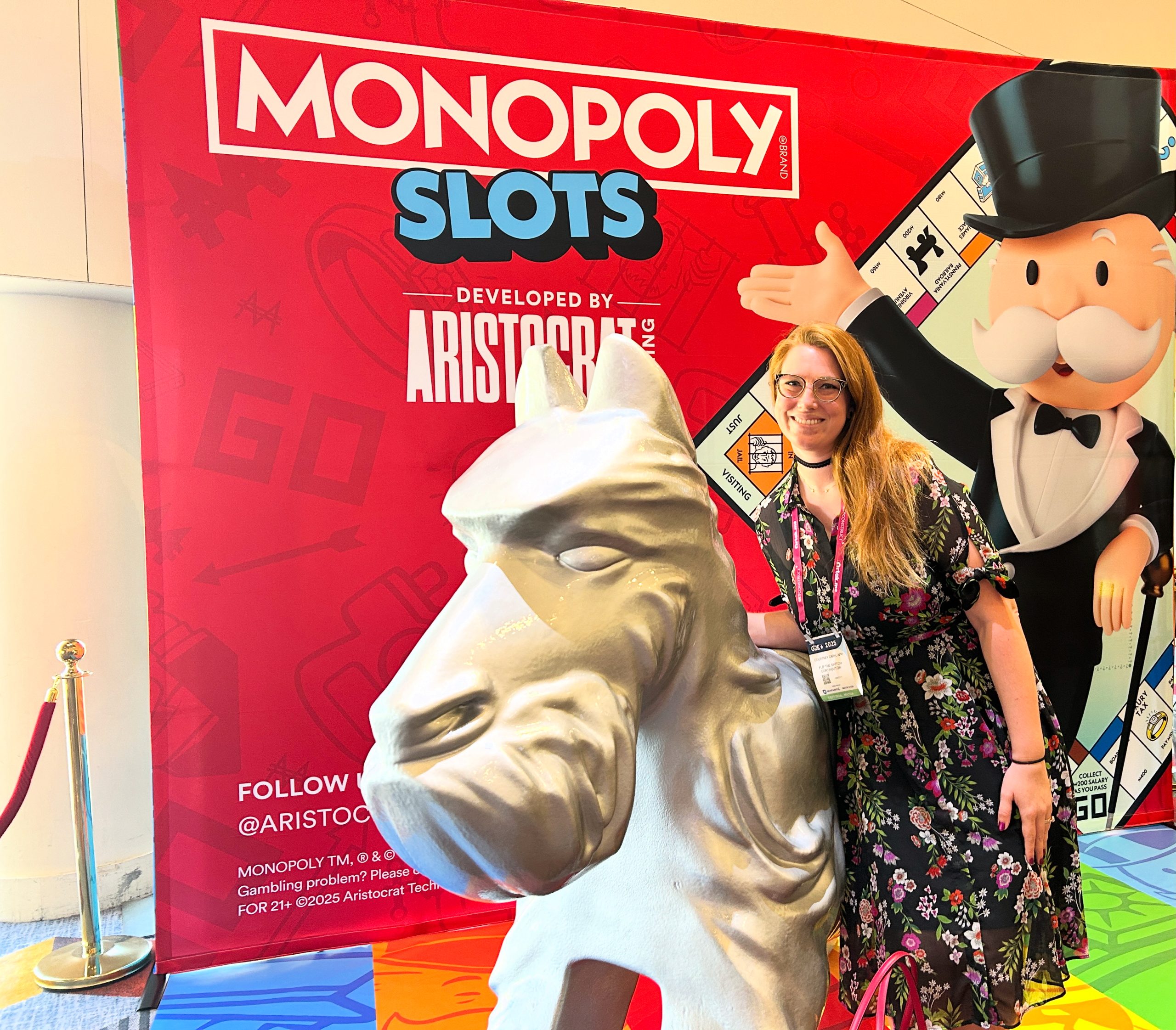 Contributor Courtney Car stands with the scotty dog trumpeting the upcoming Monopoly Slots relationship with Aristorcat Gaming.